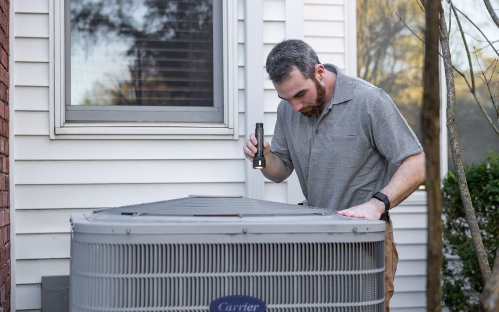 Technician inspecting an outdoor HVAC unit before the cooling season